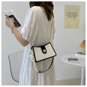Detail of white embossed chain bag with black flap and decorative silk scarf accessory