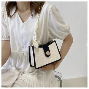 Detail of cream bag with black trim featuring cartoon embossed patterns and silk scarf strap