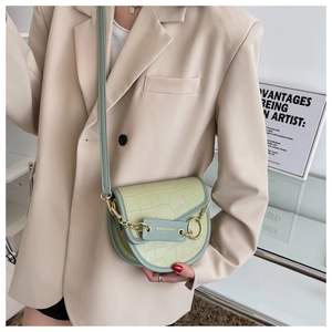 Detail of light green crocodile embossed saddle bag with gold chain and metal hardware