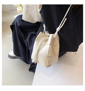 Detail of hand-woven cream bucket bag featuring textured lattice pattern and knot strap