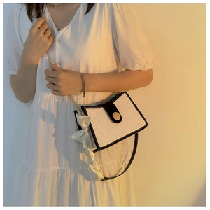 Detail of white rectangular shoulder bag with heart embossments and silk scarf on chain