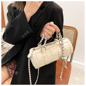 Detail of off-white woven barrel bag with silver metal chain strap held by a model