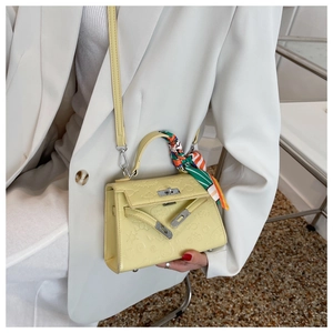 Detail of light yellow Kelly bag featuring cartoon embossing and a silk scarf on the handle