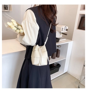 Detail showing the cream woven bucket bag with drawstring closure and knotted strap