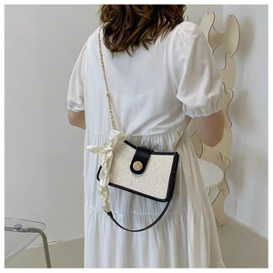 Detail of white embossed crossbody bag with gold chain strap and decorative scarf