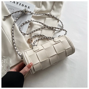 Detail of a beige woven cylinder bag with a chunky metal chain strap on an aesthetic background
