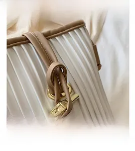 Detail of white pleated handbag with brown leather trim and golden T-shaped metal buckle