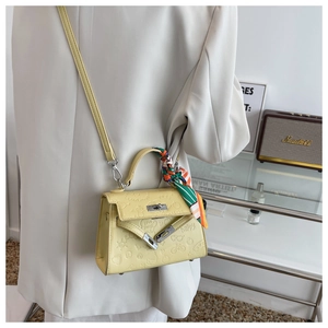 Detail of light yellow embossed leather bag with silk scarf on handle and silver lock