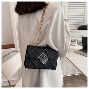 Détail d'un sac matelassé noir avec serrure dorée sur un mannequin en costume blanc