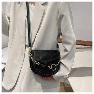 Detail of black crocodile texture saddle bag with gold metal chain and logo tag