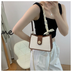Detail of white graffiti crossbody bag with brown trim and silk scarf wrapped strap