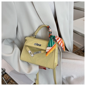Close-up of yellow embossed leather handbag with silk scarf handle and silver twist lock