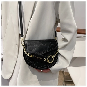 Detail of black faux crocodile saddle bag featuring bold gold chain and flap closure