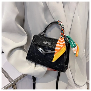 Detail of embossed black leather handbag with decorative silk scarf and metallic twist lock