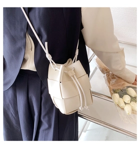 Close-up of a white woven bucket bag worn as a crossbody with casual blue attire