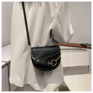 Detail of black crocodile pattern saddle bag with gold chain and logo tag on white blazer