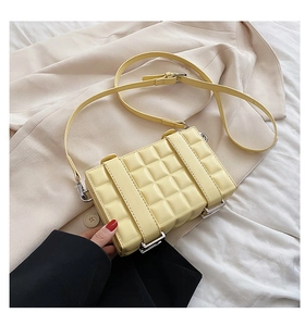 Detail of light yellow quilted square bag with silver metal lock on a beige blazer