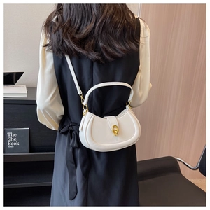 Close-up of a white half-moon PU leather handbag with a gold metal lock and leather strap