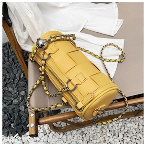 Close-up of yellow woven leather barrel bag with silver chain and metal ball charm