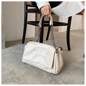 Detailansicht der beigen gesteppten Ledertasche mit Kettenriemen auf minimalistischem Stuhl