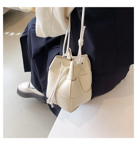 Detail of a creamy white woven bucket bag showing its textured faux leather and drawstring
