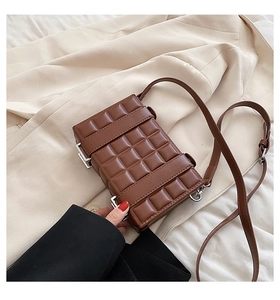 Detail of a brown quilted crossbody bag with chocolate block texture on beige blazer