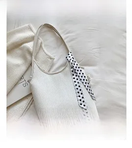 Detailed view of white pleated shoulder bag with black and white polka dot ribbon accent