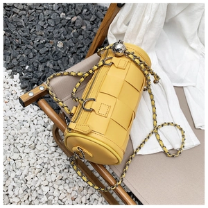 Detail of yellow woven barrel bag featuring chunky chain strap and silver ball charm