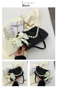 Détail du sac plissé noir avec anse en perles, chaîne dorée et nœud en satin