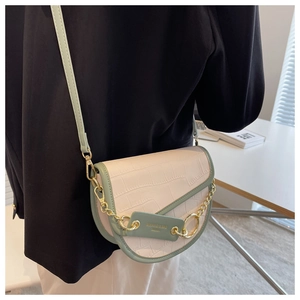 Detail of a pink croc-embossed saddle bag with sage green trim and gold chain accent