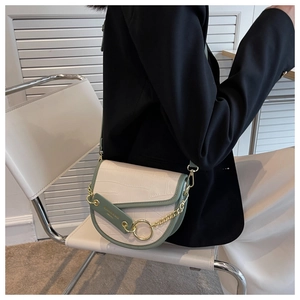 Detail of crossbody saddle bag with crocodile texture and gold ring on a black blazer
