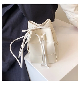 Detail view of the woven leather texture and cream drawstring closure on the bucket bag