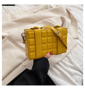 Macro detail of yellow textured plaid crossbody bag with decorative straps on beige fabric