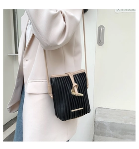 Detail of black pleated crossbody bag with beige trim and golden T-shaped metal buckle