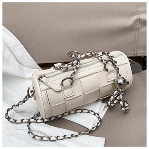 Close-up of woven cream cylinder bag with chunky silver chain and metal ball charm