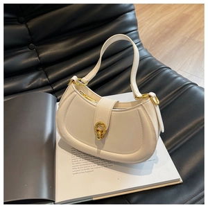 Close-up of a white semi-circle leather handbag with elegant gold hardware on a book
