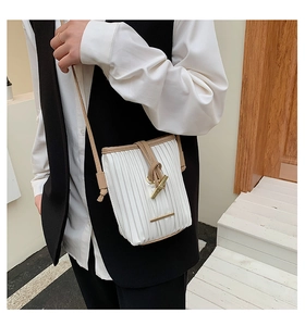 Detail of white pleated bucket bag featuring gold metal buckle and beige trim strap