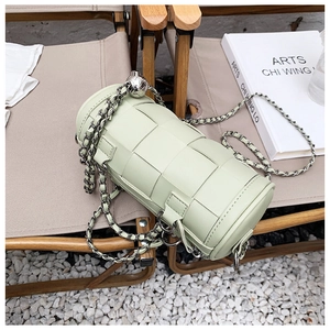 Close-up of light green woven barrel bag with silver chain and metal ball on a chair