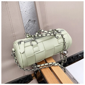 Detailed view of light green woven cylinder bag with silver chain and metal ball ornament
