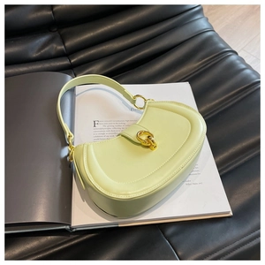 Close-up of a light green leather crescent bag with golden buckle on an art magazine