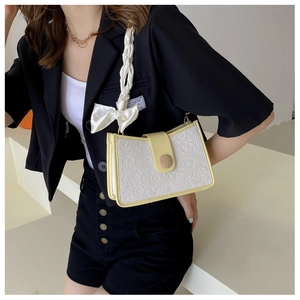 Detail of cream crossbody bag with colorful embossed patterns and a silk ribbon handle