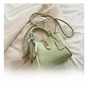 Dettaglio borsa a secchiello verde chiaro in pelle con chiusura dorata e foulard