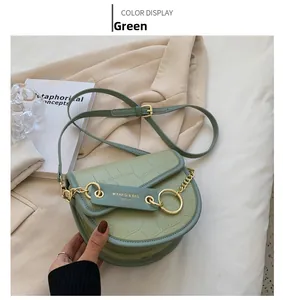 Close-up of green crocodile-textured saddle bag with gold chain on beige blazer