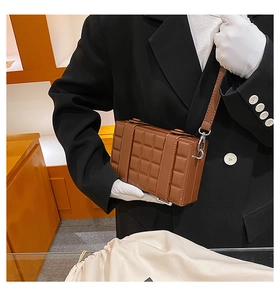 Detail of brown box crossbody bag with textured checkered pattern and silver metal hooks