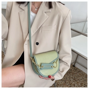 Detail of green crocodile texture saddle bag with gold chain on model in neutral room