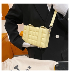 Detail of a chic yellow plaid crossbody box bag held by a model in a luxury setting