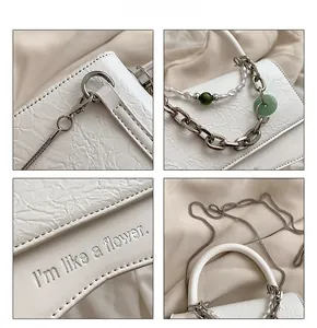 Detailed view of white textured crossbody bag with pearl and green bead chain