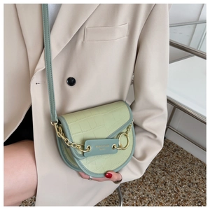 Detail view of light green saddle bag with crocodile texture and gold chain ornament