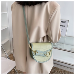 Light green crocodile pattern saddle bag with gold metal ring detail on beige blazer
