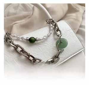 Detail of silver chain strap with baroque pearls and green charms on a white bag